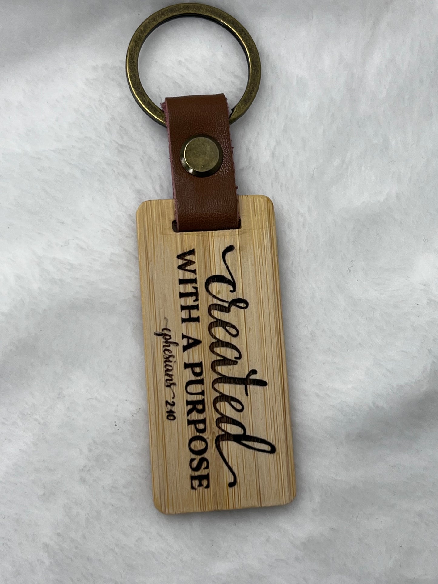 A wooden keychain with a leather strap, metal ring, and the inscription 'Created with a purpose Eph. 2:40'.